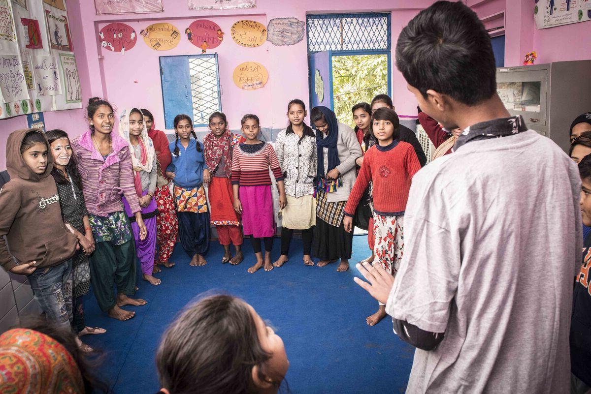 Man talking to a group of children in a room with pink walls 